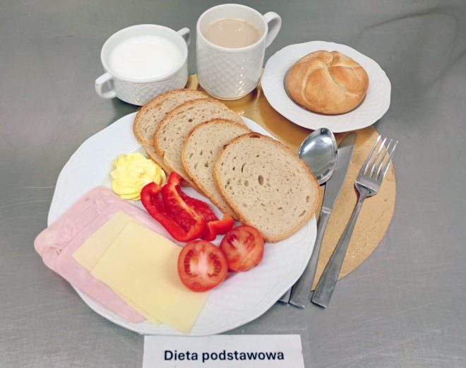 Posiłek diety podstawowej: kromki pieczywa, wędlina, ser żółty, masło, papryka i pomidor, podane z bułką oraz napojami gorącymi