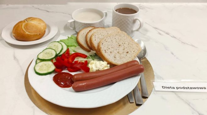 Śniadanie w diecie podstawowej: parówki, pieczywo pszenne, świeże warzywa, masło i ketchup. Posiłek uzupełniają kawa oraz mleko