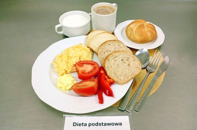 Śniadanie w diecie podstawowej: jajecznica, świeże pieczywo pszenne, pomidor, papryka, porcja masła oraz ciepłe napoje – kawa i mleko. Całość podana na białej zastawie
