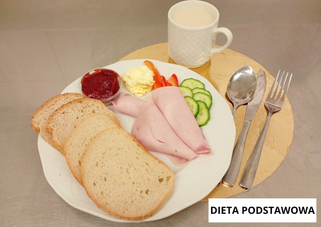 Śniadanie w diecie podstawowej: pieczywo pszenne, wędlina drobiowa, masło, dżem, świeże warzywa oraz mleko, podane na białej zastawie