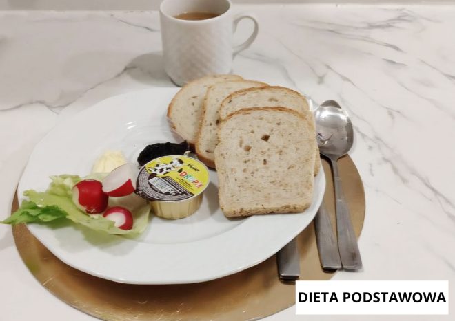 Śniadanie w diecie podstawowej: pieczywo pszenne, serek topiony, masło, sałata i rzodkiewka. Obok kubek z herbatą. Na zdjęciu widoczny napis „Dieta podstawowa”