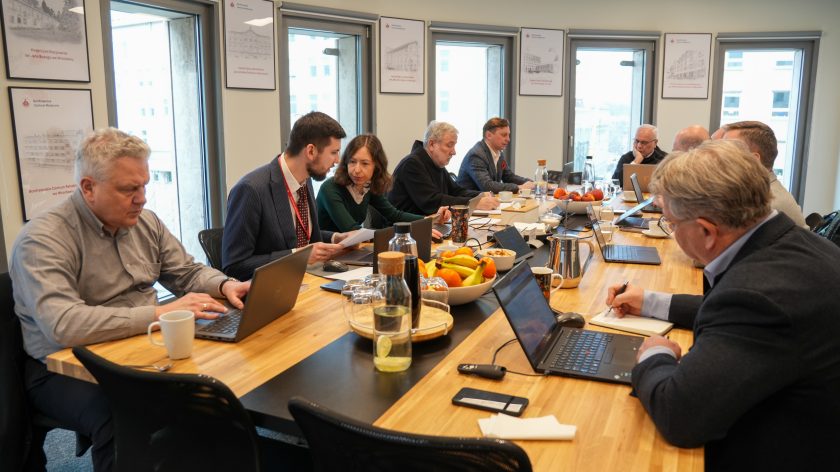 Uczestnicy narady przy długim stole konferencyjnym w Bonifraterskim Centrum Medycznym – rozmowy i praca przy laptopach podczas spotkania roboczego