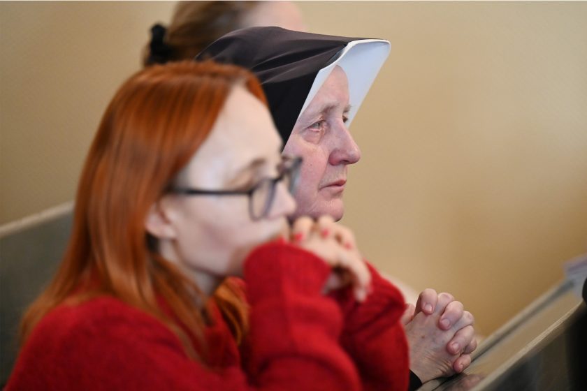 Zbliżenie na twarze dwóch kobiet siedzących w ławce – na pierwszym planie kobieta w czerwonym swetrze, w tle siostra zakonna w czarnym habicie; obie skupione i zamyślone podczas modlitwy