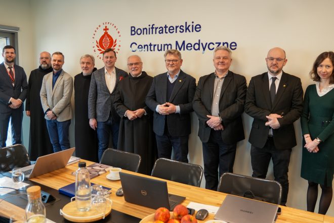 Grupowe zdjęcie uczestników spotkania w Bonifraterskim Centrum Medycznym – przedstawiciele szpitala i zaproszeni goście stoją w sali konferencyjnej pod logo placówki