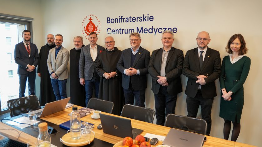 Grupowe zdjęcie uczestników spotkania w Bonifraterskim Centrum Medycznym – przedstawiciele szpitala i zaproszeni goście stoją w sali konferencyjnej pod logo placówki