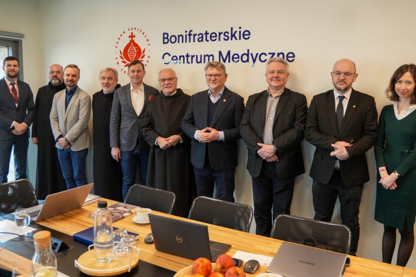Grupowe zdjęcie uczestników spotkania w Bonifraterskim Centrum Medycznym – przedstawiciele szpitala i zaproszeni goście stoją w sali konferencyjnej pod logo placówki
