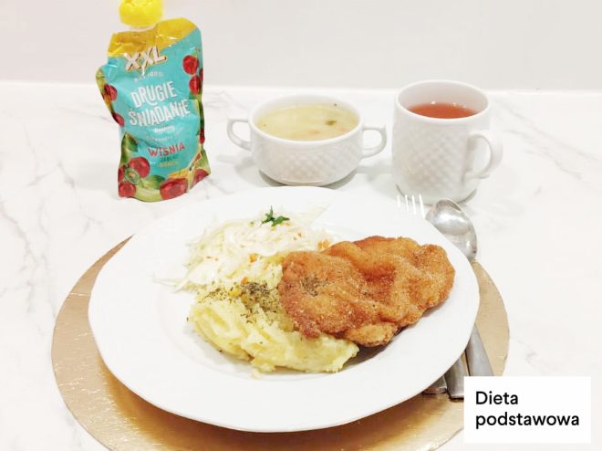 Obiad w diecie podstawowej: panierowany kotlet, puree ziemniaczane oraz surówka z białej kapusty. W tle miseczka zupy i kubek herbaty oraz mus owocowy