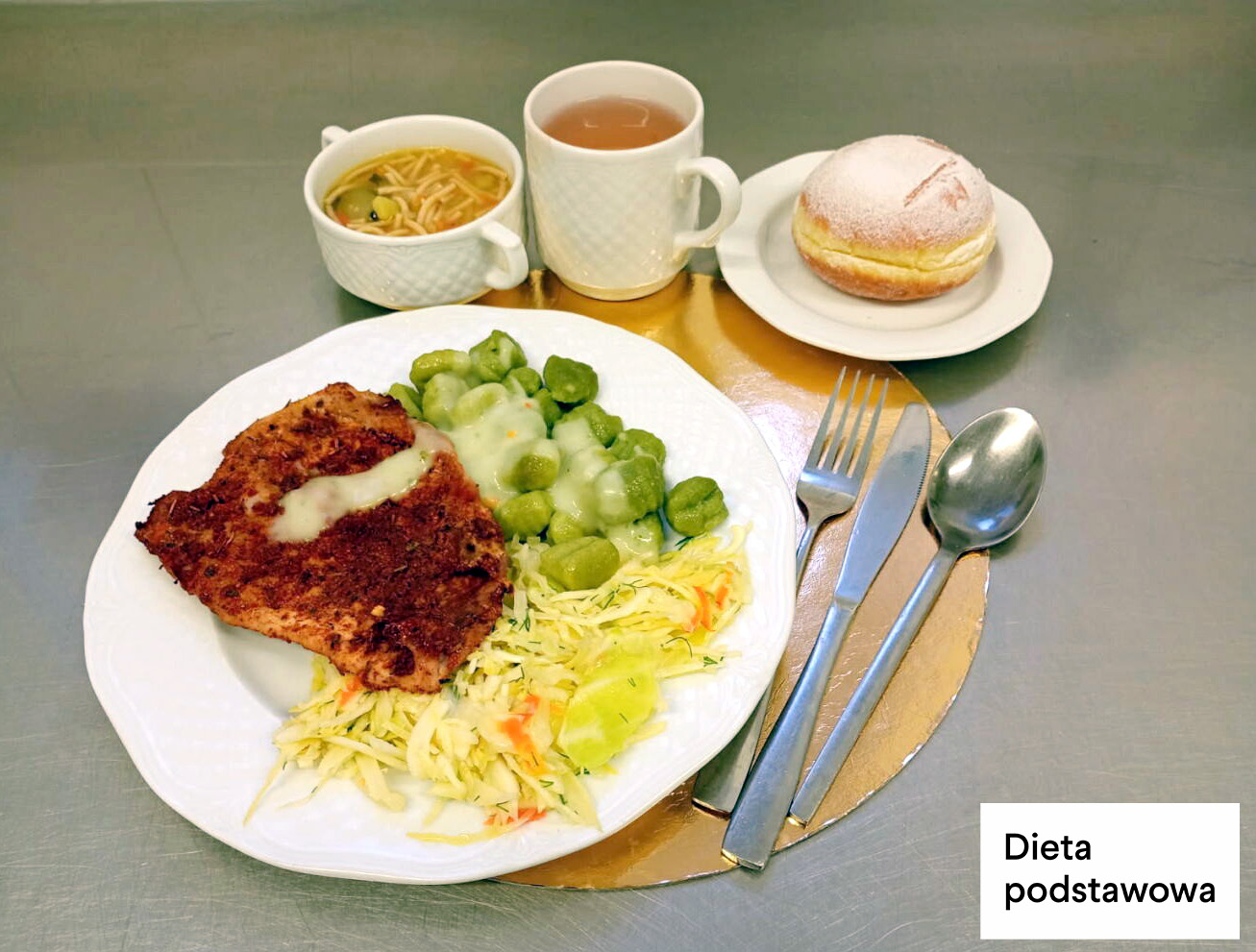 Obiad w diecie podstawowej: kotlet panierowany z sosem, kopytka, surówka z kapusty oraz brukselka w sosie. Dodatkowo rosół z makaronem, herbata i pączek z nadzieniem