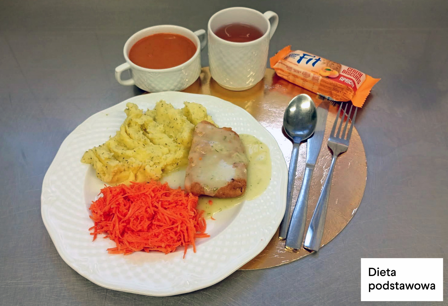 Obiad w diecie podstawowej: kotlet drobiowy w sosie koperkowym, puree ziemniaczane z koperkiem oraz surówka z tartej marchewki. Dodatkowo herbata, zupa pomidorowa oraz herbatniki