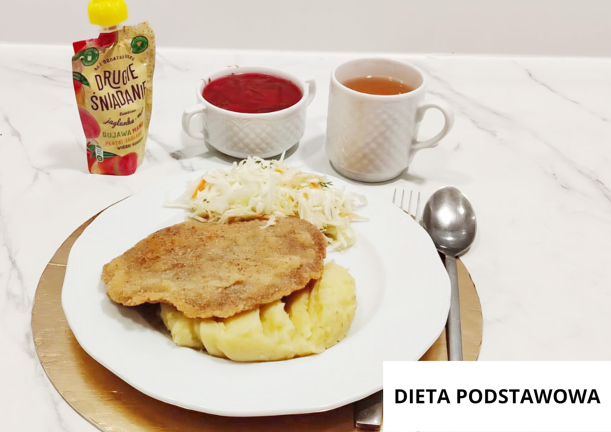 Kotlet schabowy w panierce podany z puree ziemniaczanym oraz surówką z białej kapusty. W tle filiżanka czerwonej zupy, kubek herbaty oraz mus owocowy w tubce. Nakrycie ustawione na złotej podkładce