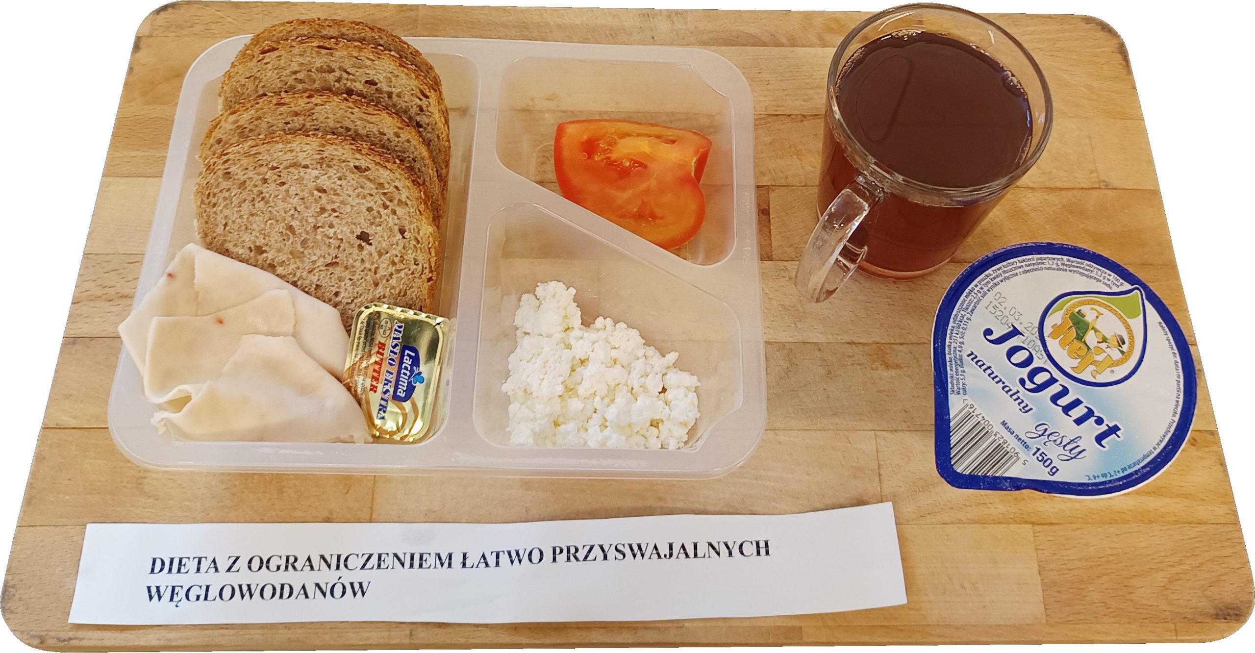 Śniadanie w diecie z ograniczeniem łatwo przyswajalnych węglowodanów: kromki pieczywa, plasterki wędliny drobiowej, twarożek, kawałek pomidora, jogurt oraz herbata