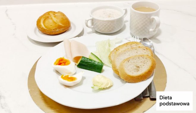 Zestaw śniadaniowy w diecie podstawowej: jajko na twardo, plasterki wędliny, świeży ogórek, pieczywo oraz dodatki warzywne. Podany z napojem i kaszą manną