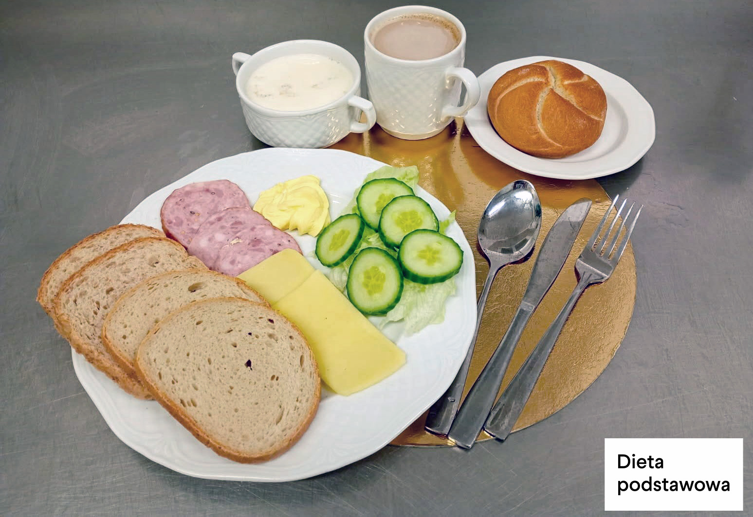 Śniadanie w diecie podstawowej: trzy kromki chleba pszenno-żytniego, masło, serek kanapkowy, sałata z rzodkiewką, kawa z mlekiem i zupa mleczna. Obok podana bułka kajzerka