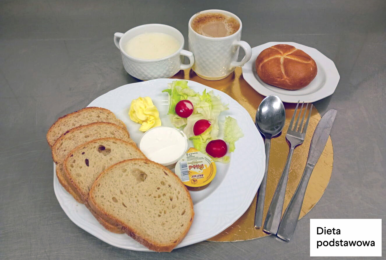 Śniadanie w diecie podstawowej: trzy kromki chleba pszenno-żytniego, masło, serek kanapkowy, sałata z rzodkiewką, kawa z mlekiem i zupa mleczna. Obok podana bułka kajzerka