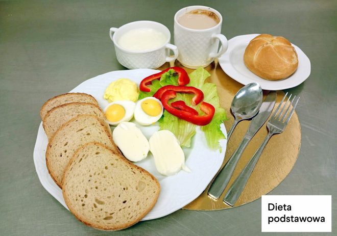 Śniadanie w diecie podstawowej: kromki pieczywa, jajko na twardo, ser mozzarella, sałata i plasterki czerwonej papryki. Obok bułka oraz napoje mleczne