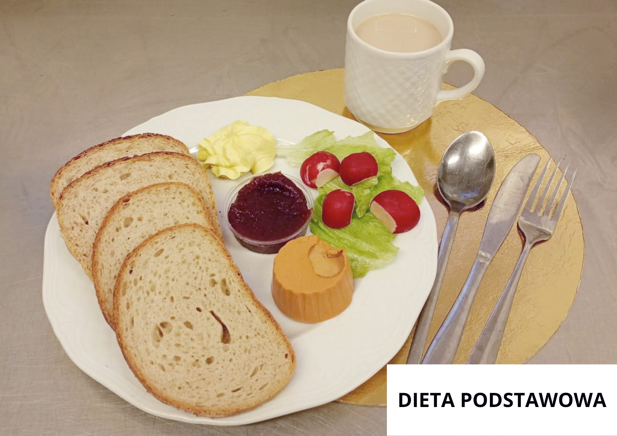 Na białym talerzu trzy kromki chleba, porcja masła, pasztet drobiowy w krążku, buraczki w małym pojemniku oraz kilka rzodkiewek na liściu sałaty. W tle kubek kawy z mlekiem. Sztućce ułożone po prawej stronie