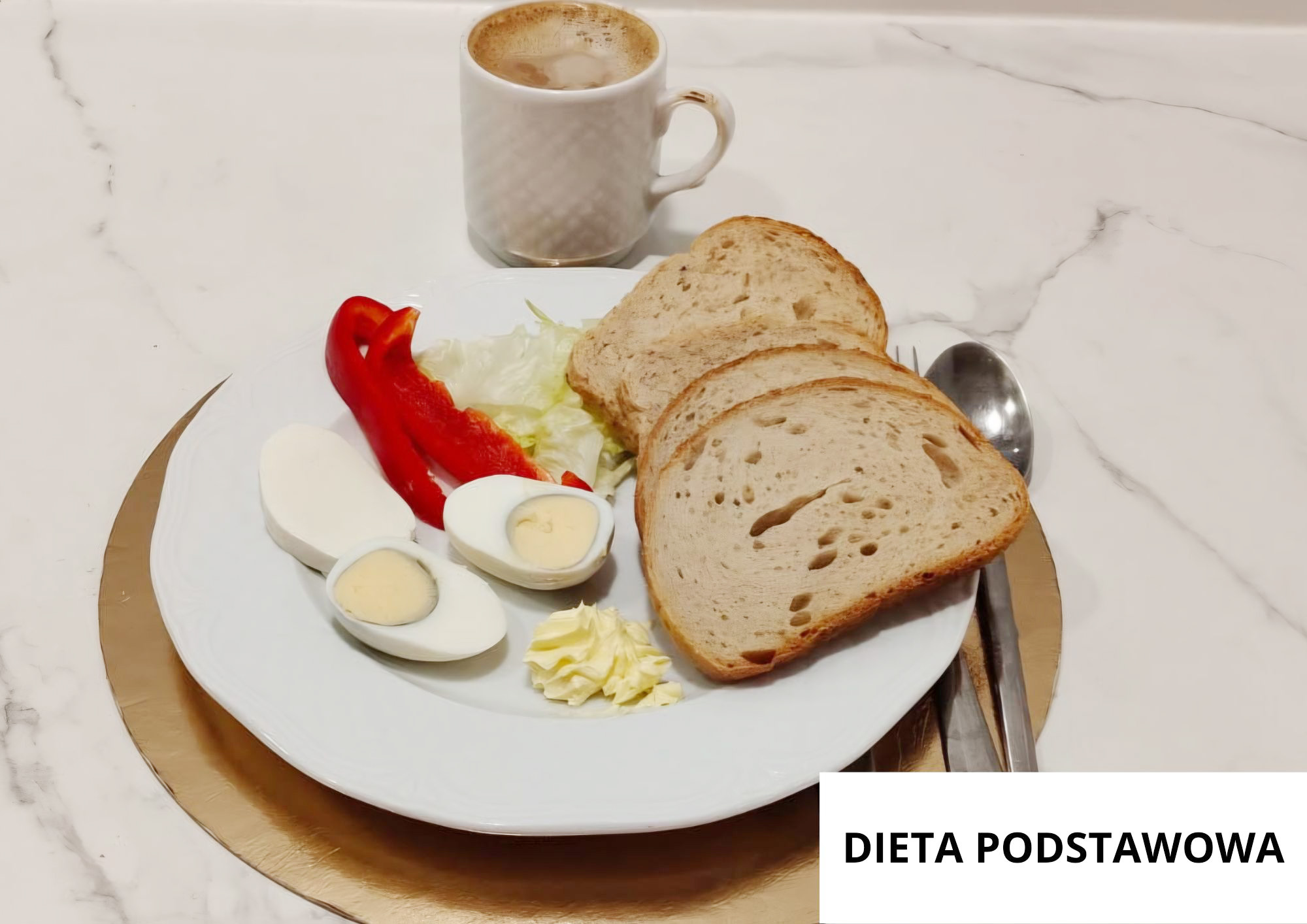 Na talerzu trzy kromki chleba, jajko gotowane na twardo przekrojone na połówki, plaster czerwonej papryki, liście sałaty oraz porcja masła. W tle kubek kawy z mlekiem. Nakrycie ustawione na złotej podkładce