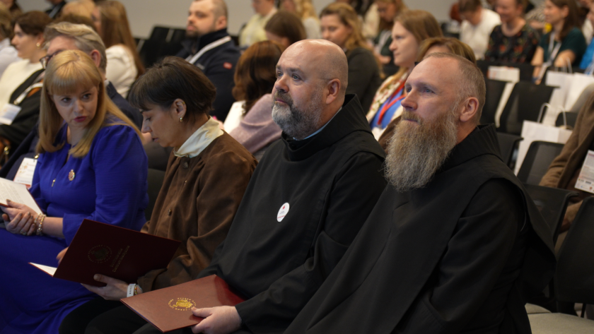 Uczestnicy sympozjum siedzą na sali konferencyjnej i słuchają prelekcji. W pierwszym rzędzie widoczni są bracia bonifratrzy w habitach oraz uczestnicy wydarzenia z materiałami konferencyjnymi