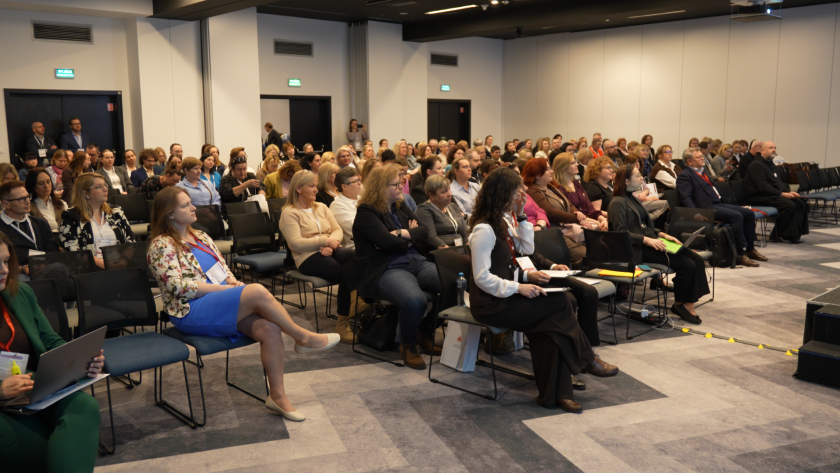 Szerokie ujęcie sali konferencyjnej wypełnionej uczestnikami sympozjum hospicyjnego słuchającymi wykładu. Wśród publiczności znajdują się pracownicy ochrony zdrowia, przedstawiciele instytucji oraz bracia bonifratrzy