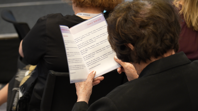 Uczestniczka sympozjum siedzi na sali konferencyjnej i czyta program wydarzenia wydrukowany w materiałach konferencyjnych