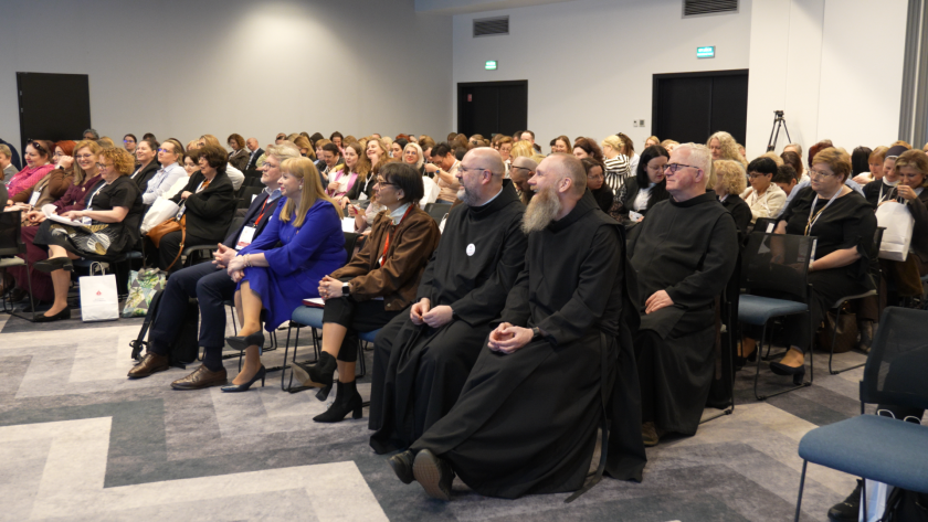 Uczestnicy sympozjum siedzą na sali konferencyjnej i słuchają wystąpień. W pierwszym rzędzie widoczni są bracia bonifratrzy w habitach oraz zaproszeni goście
