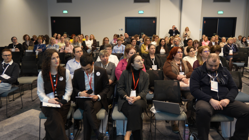 Widok sali konferencyjnej wypełnionej uczestnikami sympozjum hospicyjnego. W pierwszym rzędzie siedzą osoby prowadzące dyskusję oraz uczestnicy z mikrofonami i materiałami konferencyjnymi