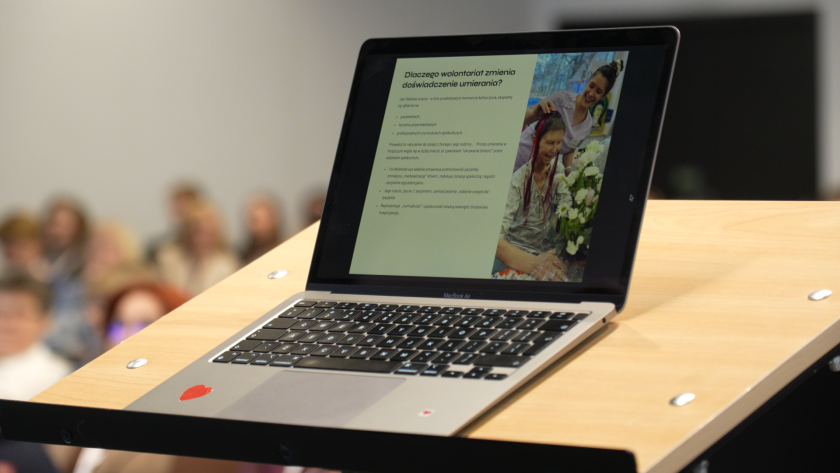 Laptop ustawiony na mównicy wyświetla slajd prezentacji dotyczącej wolontariatu i doświadczenia umierania podczas wykładu
