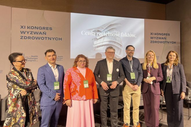 Siedmioro uczestników panelu stoi na scenie podczas XI Kongresu Wyzwań Zdrowotnych; w tle widoczne są banery wydarzenia i ekran z napisem „Cenią rzetelność faktów”