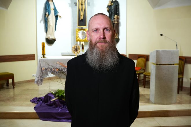 Brat Paweł Kulka w czarnym habicie zakonnym stoi w kaplicy przed ołtarzem; w tle widoczny jest krucyfiks, tabernakulum oraz figury Matki Bożej i świętego