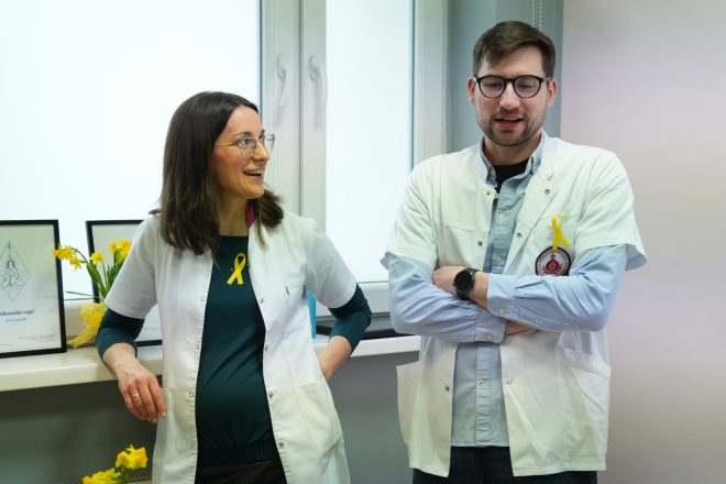 Dwoje pracowników medycznych w białych fartuchach rozmawia podczas spotkania edukacyjnego, oboje mają przypięte żółte wstążki