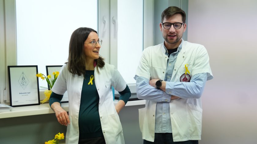 Dwoje pracowników medycznych w białych fartuchach rozmawia podczas spotkania edukacyjnego, oboje mają przypięte żółte wstążki