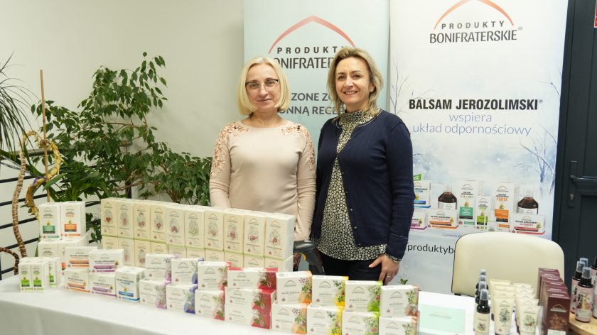 Dwie kobiety prezentują produkty bonifraterskie na stoisku promocyjnym, w tle roll-up z informacją o Balsamie Jerozolimskim