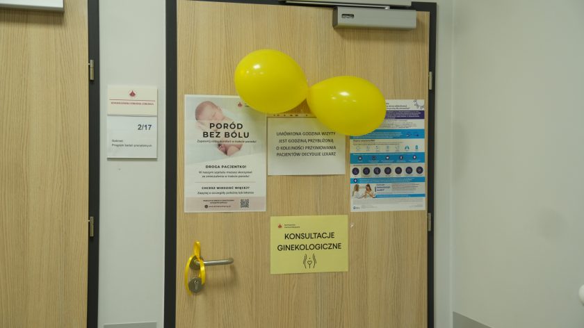 Drzwi gabinetu ginekologicznego oznaczone numerem 2/17, ozdobione żółtymi balonami i informacjami dla pacjentek, w tym plakatem „Poród bez bólu” i kartką „Konsultacje ginekologiczne”