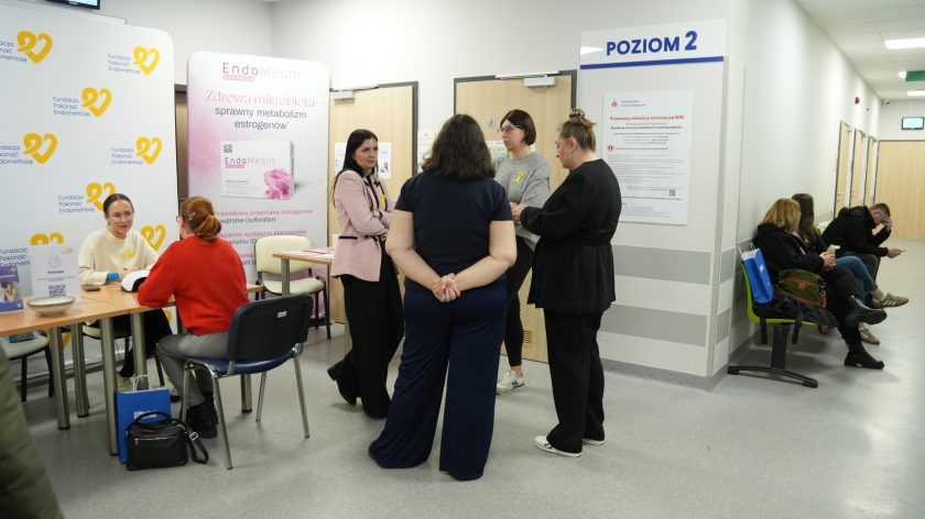 Korytarz placówki medycznej z punktem konsultacyjnym Fundacji Pokonać Endometriozę; kilka kobiet rozmawia, inne siedzą na ławkach i czekają na wizytę