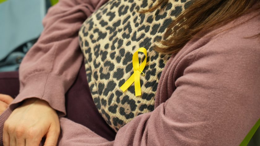 Zbliżenie na tors uczestniczki spotkania w swetrze w panterkę i różowym kardiganie, z przypiętą żółtą wstążką symbolizującą solidarność i wsparcie