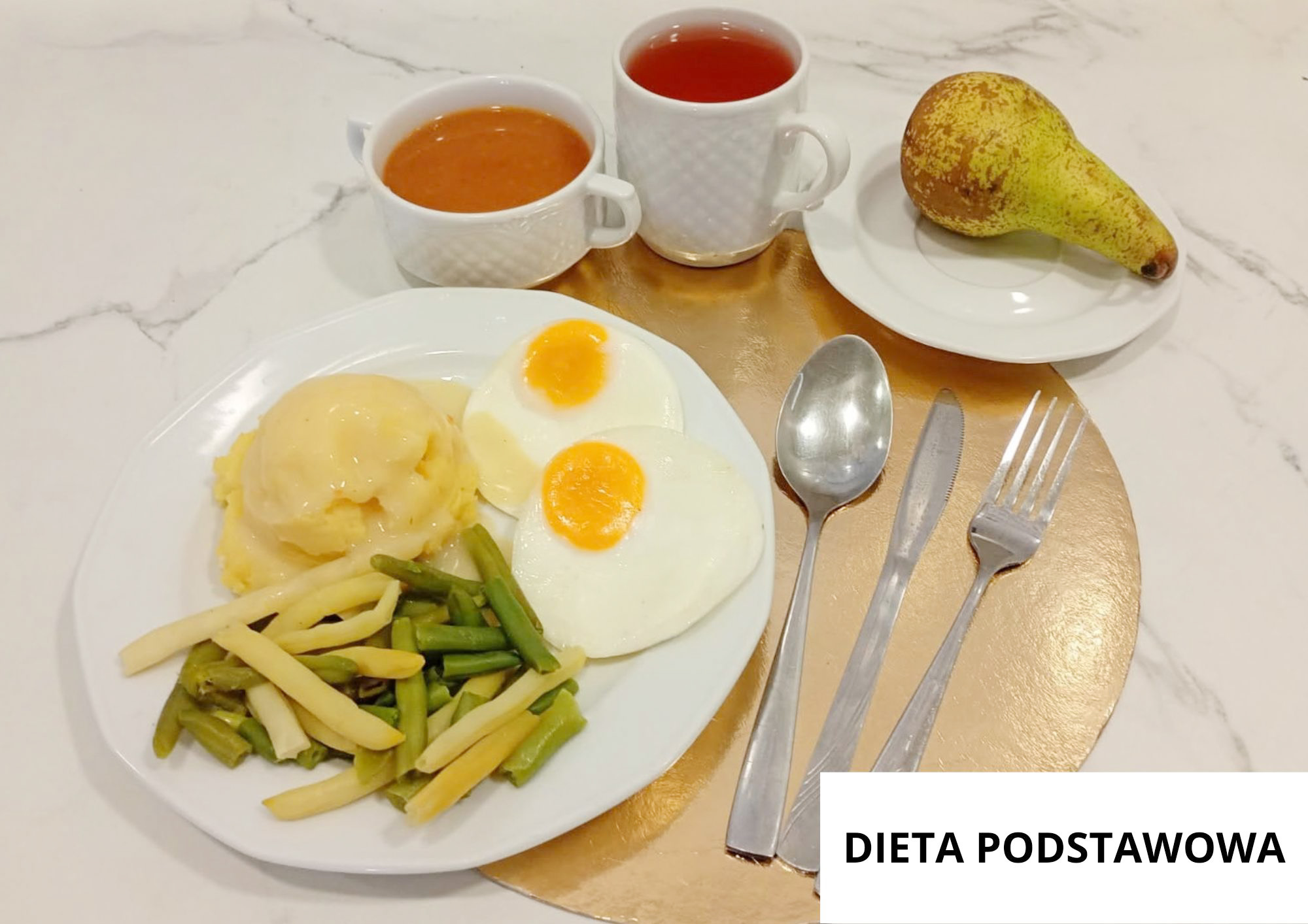 Na białym talerzu podano dwa jajka sadzone, puree ziemniaczane z jasnym sosem oraz gotowaną fasolkę szparagową zieloną i żółtą. Nad talerzem stoją dwie białe filiżanki z napojami, a na osobnym talerzyku leży gruszka. Obok leżą łyżka, nóż i widelec. W prawym dolnym rogu znajduje się napis „DIETA PODSTAWOWA”