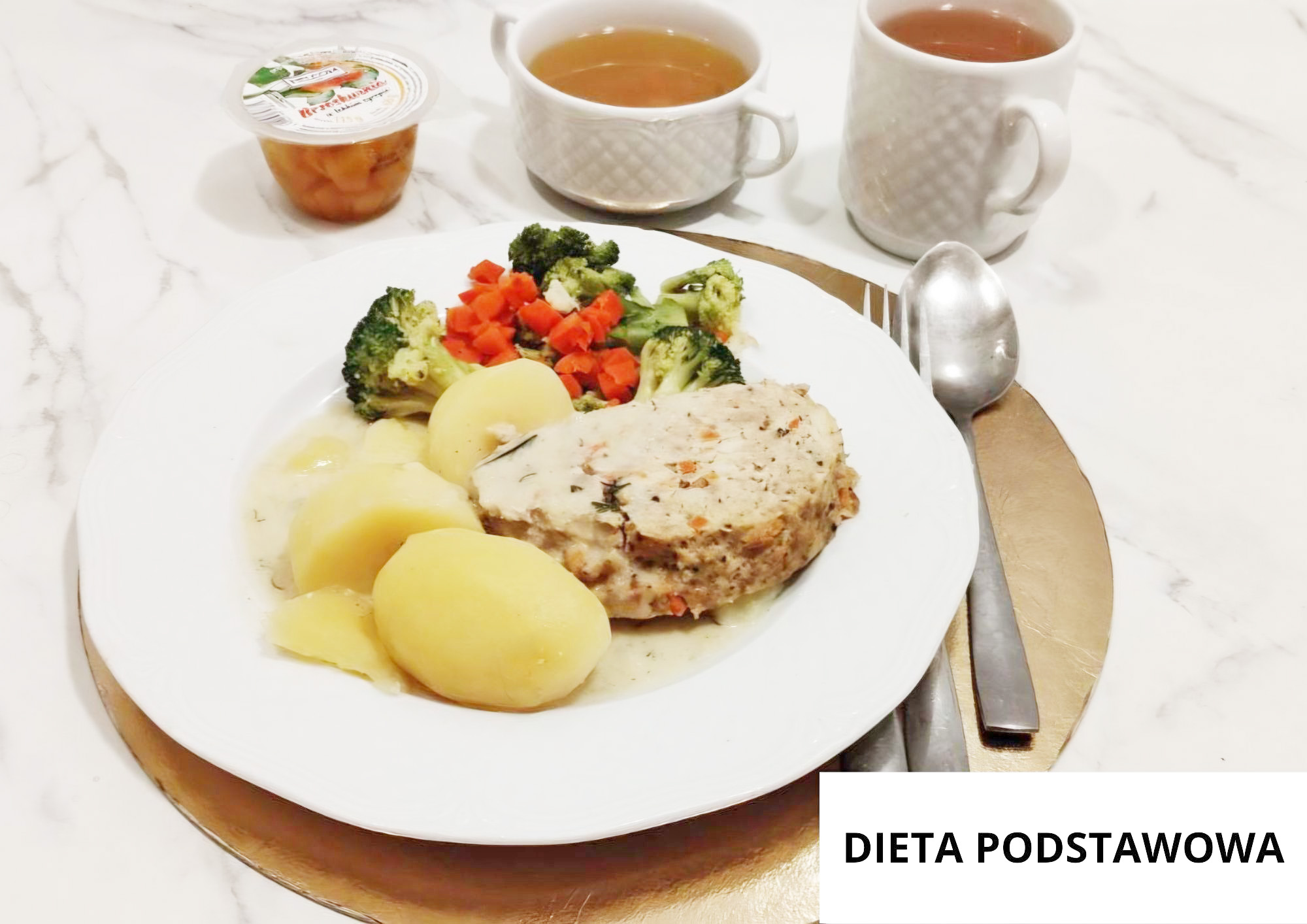 Na białym talerzu ustawionym na złotej podkładce podano porcję gotowanych ziemniaków polanych jasnym sosem oraz plaster pieczonego mięsa z widocznymi ziołami. Obok mięsa znajduje się porcja gotowanych warzyw – brokuły i drobno pokrojona marchewka. W tle ustawiono białą filiżankę z klarownym bulionem, kubek z herbatą oraz mały kubeczek z kompotem owocowym. Po prawej stronie talerza leżą sztućce. W prawym dolnym rogu widoczny napis „DIETA PODSTAWOWA”