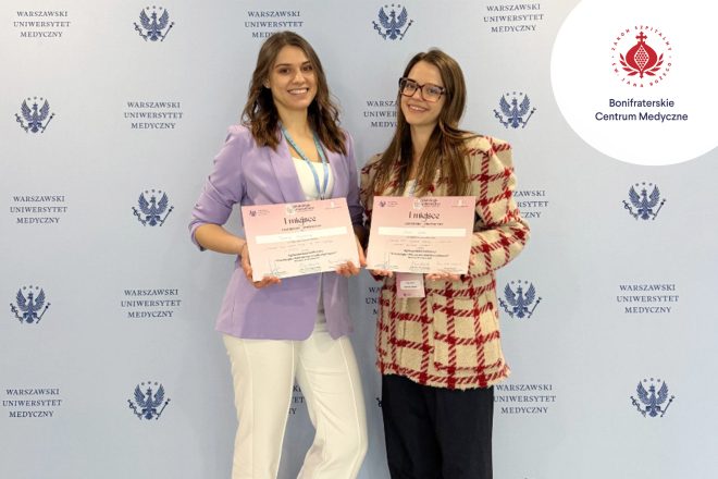 Dwie młode kobiety pozują na tle ścianki Warszawskiego Uniwersytetu Medycznego, trzymając dyplomy za zajęcie pierwszego miejsca. Uśmiechnięte laureatki prezentują nagrody, mają na sobie identyfikatory konferencyjne, a obok widoczny jest logotyp Bonifraterskiego Centrum Medycznego
