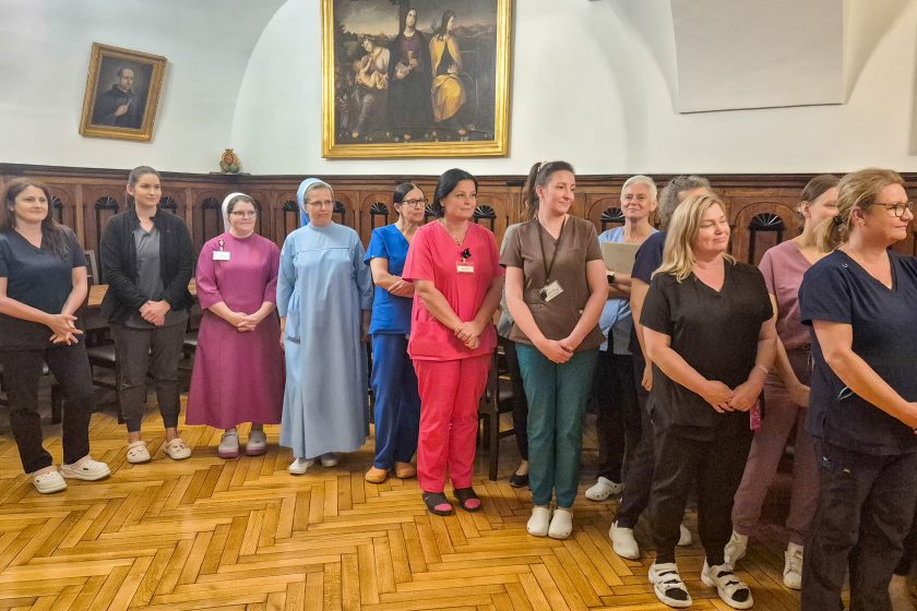 Pracownicy Szpitala Zakonu Bonifratrów św. Jana Grandego w Krakowie oraz siostry zakonne stoją w zabytkowej sali z drewnianą boazerią podczas uroczystego spotkania
