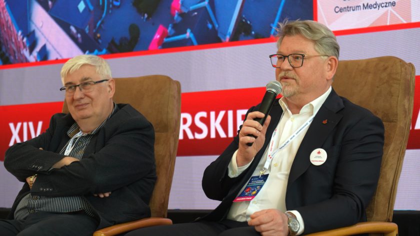 Dwóch uczestników panelu dyskusyjnego siedzi w fotelach na scenie konferencyjnej. Mężczyzna po prawej stronie przemawia do mikrofonu, a za nimi widoczny jest ekran z prezentacją dotyczącą Bonifraterskiego Centrum Medycznego oraz Bonifraterskich Spotkań z Rehabilitacją