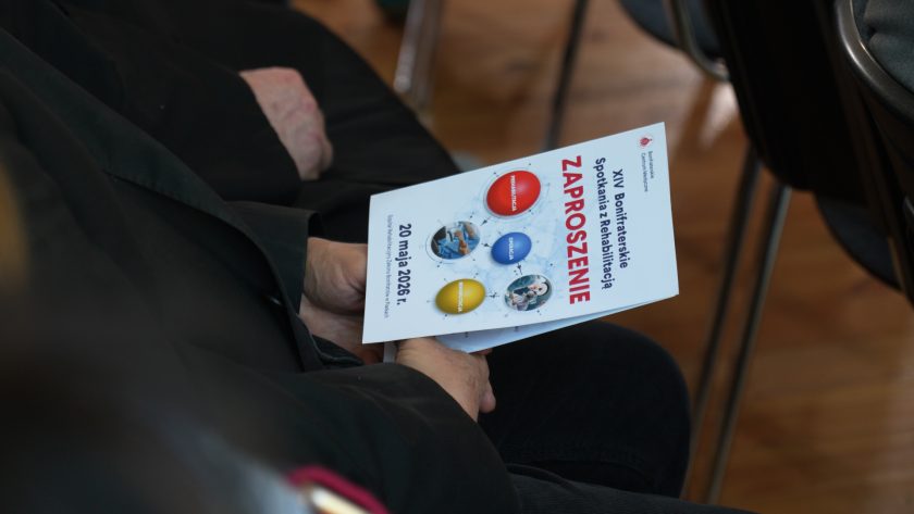 Zbliżenie na dłonie uczestnika trzymającego program XIII Bonifraterskich Spotkań z Rehabilitacją. Na okładce widoczna jest data 20 maja 2025 roku oraz grafiki odnoszące się do rehabilitacji, opieki i medycyny