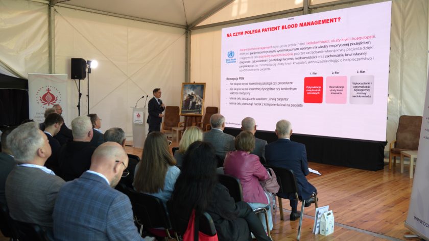 Prelegent prowadzi wykład na temat Patient Blood Management. Na dużym ekranie widoczny jest slajd omawiający trzy filary postępowania: optymalizację masy krwinek czerwonych, minimalizację utraty krwi i wykorzystanie fizjologicznej rezerwy niedokrwistości
