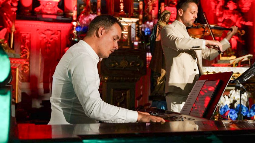 Muzycy wykonują utwór instrumentalny podczas koncertu. Na pierwszym planie pianista gra na instrumencie klawiszowym, a obok skrzypek prezentuje partię solową