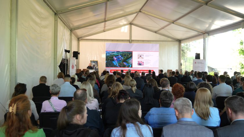 Wnętrze namiotu konferencyjnego wypełnionego uczestnikami wydarzenia. Publiczność siedzi w rzędach i obserwuje prezentację wyświetlaną na dużym ekranie. Na scenie widoczny jest prelegent oraz grafika XIV Bonifraterskich Spotkań z Rehabilitacją