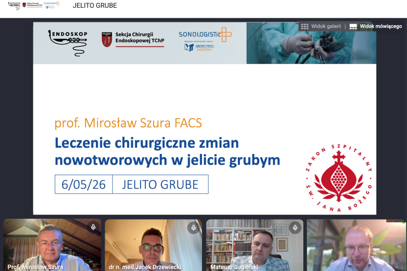 Zrzut ekranu z internetowego webinaru medycznego poświęconego chirurgicznemu leczeniu zmian nowotworowych w jelicie grubym. W centralnej części widoczny jest slajd prezentacji z białym tłem i granatowym nagłówkiem „JELITO GRUBE”. Na slajdzie znajdują się logotypy Endoskop 2026, Sekcji Chirurgii Endoskopowej TChP oraz firmy Sonologistic. Po prawej stronie baneru widoczne jest zdjęcie lekarza wykonującego badanie endoskopowe. Główny tytuł prezentacji zapisany dużymi niebieskimi literami brzmi: „Leczenie chirurgiczne zmian nowotworowych w jelicie grubym”. Nad nim umieszczono nazwisko prelegenta: „prof. Mirosław Szura FACS”. W dolnej części slajdu znajduje się data „6/05/26” oraz napis „JELITO GRUBE”. Po prawej stronie widoczne jest czerwone logo Szpitala św. Jana Bożego. U dołu ekranu widoczne są cztery okna uczestników spotkania online. W pierwszym oknie znajduje się prof. Mirosław Szura siedzący w pomieszczeniu z drewnianym sufitem. W drugim oknie widoczny jest dr n. med. Jacek Drzewiecki w okularach, siedzący przy biurku. W trzecim oknie pokazano Mateusza Jagielskiego na tle regału z książkami. W czwartym oknie znajduje się kolejny uczestnik spotkania siedzący w jasnym pomieszczeniu z roślinami w tle. W prawym górnym rogu slajdu znajdują się przyciski „Widok galerii” oraz „Widok mówiącego”