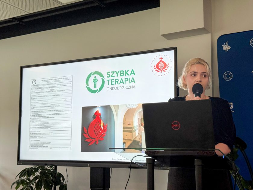 Prelegentka podczas konferencji edukacyjnej poświęconej chorobom jelita grubego prezentuje zagadnienia związane z szybką terapią onkologiczną. Na ekranie widoczne są materiały dotyczące diagnostyki i leczenia onkologicznego oraz logo Szpitala Bonifratrów w Krakowie