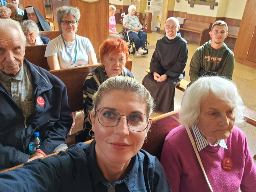 Uczestnicy spotkania pozują do wspólnego zdjęcia w ławkach kościoła. Wśród nich seniorzy, opiekunowie oraz bracia zakonni.