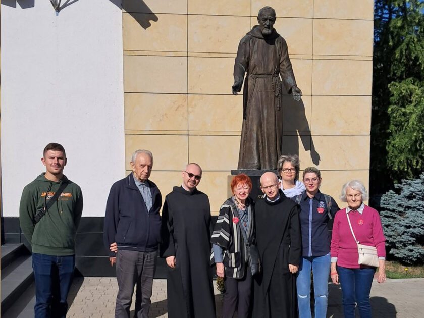 Grupa uczestników spotkania wraz z braćmi zakonnymi pozuje do wspólnego zdjęcia przed Sanktuarium Świętego Ojca Pio.