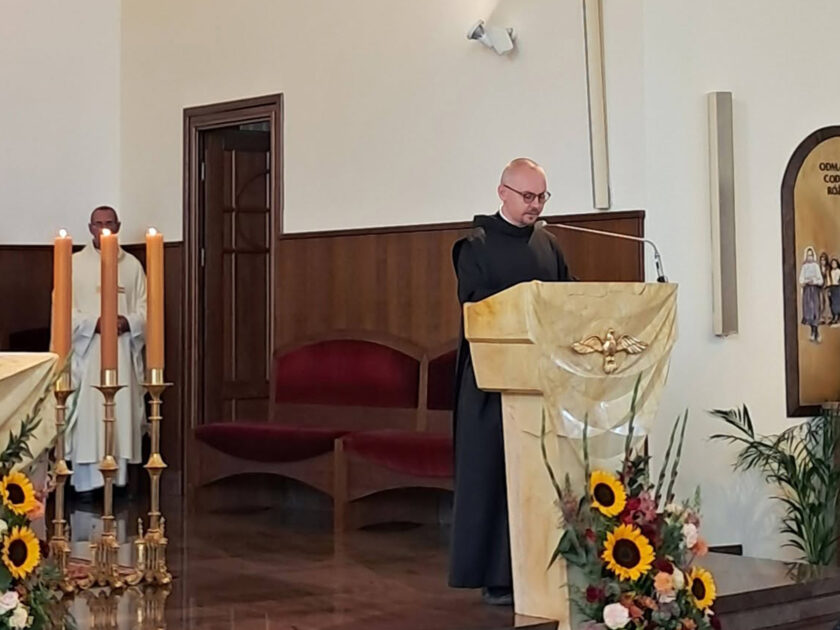 Brat zakonny czyta przy ambonie podczas nabożeństwa. Nad nim znajduje się duży wizerunek Chrystusa.