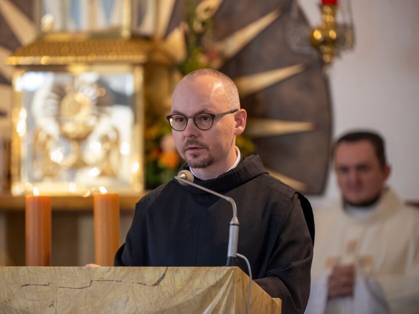 Brat zakonny przemawia przy ambonie podczas nabożeństwa. W tle widoczny ołtarz oraz drugi duchowny.